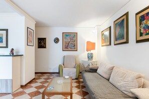 Un salon avec un sol à carreaux, un canapé, un fauteuil, une table basse et des œuvres d’art encadrées accrochées aux murs.