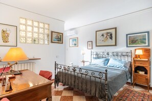 Une chambre à coucher avec un lit en métal, un bureau en bois, une chaise rouge, un tapis à motifs et divers tableaux encadrés accrochés aux murs.