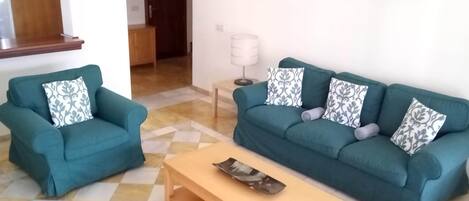 Una sala de estar con dos sofás color turquesa, una mesa de centro de madera y cojines estampados.