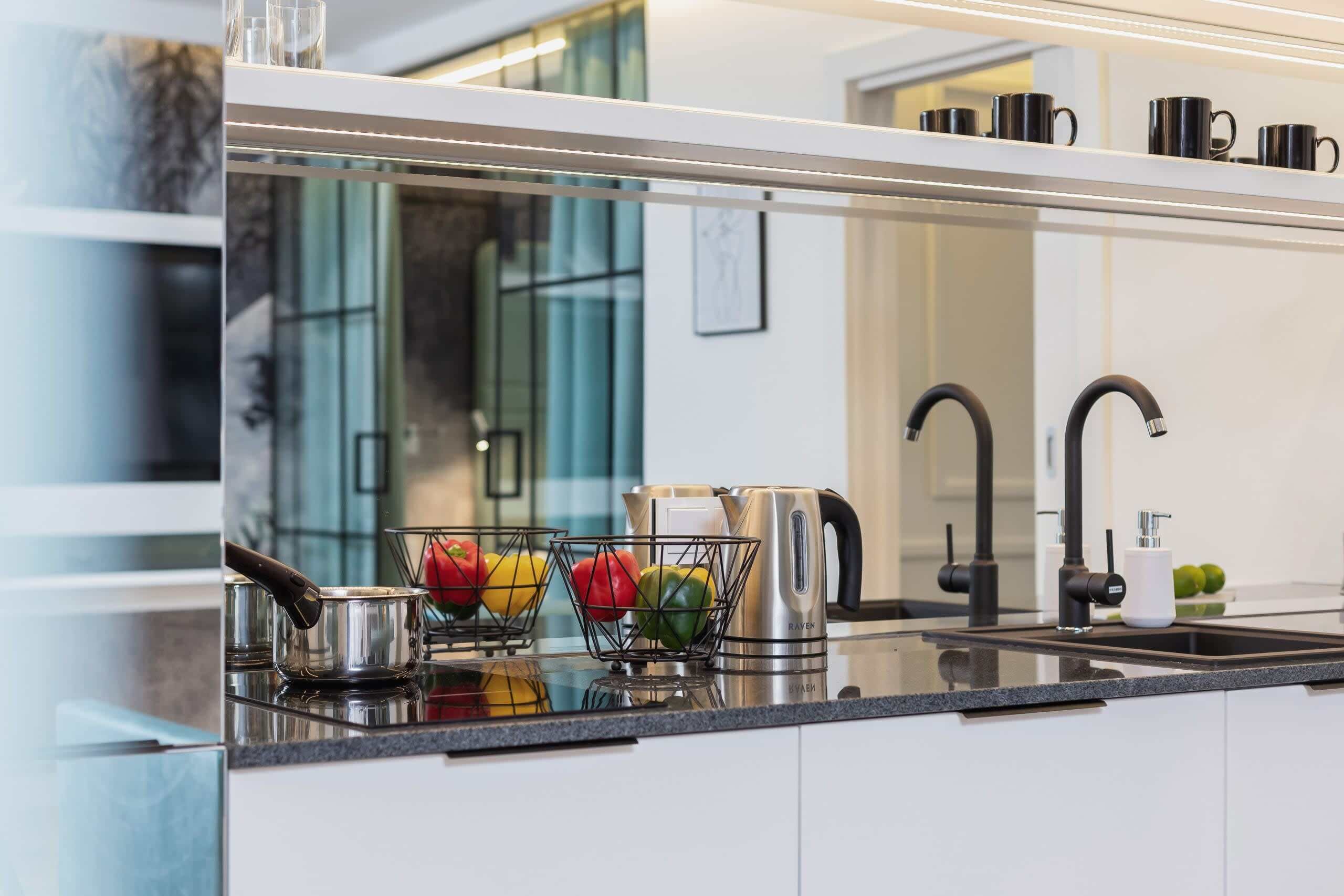 A modern kitchen with a stainless steel kettle, a fruit basket, and a coffee maker on the countertop.