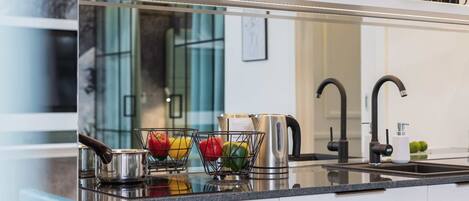 A modern kitchen with a stainless steel kettle, a fruit basket, and a coffee maker on the countertop.