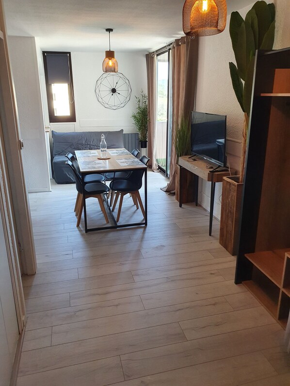 A modern living room with a dining table, sofa, TV, and large windows.