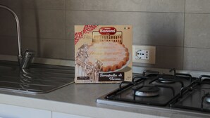 Keittiössä on kaasuliesi, pesuallas ja Bonomi-pastapakkaus työtasolla.