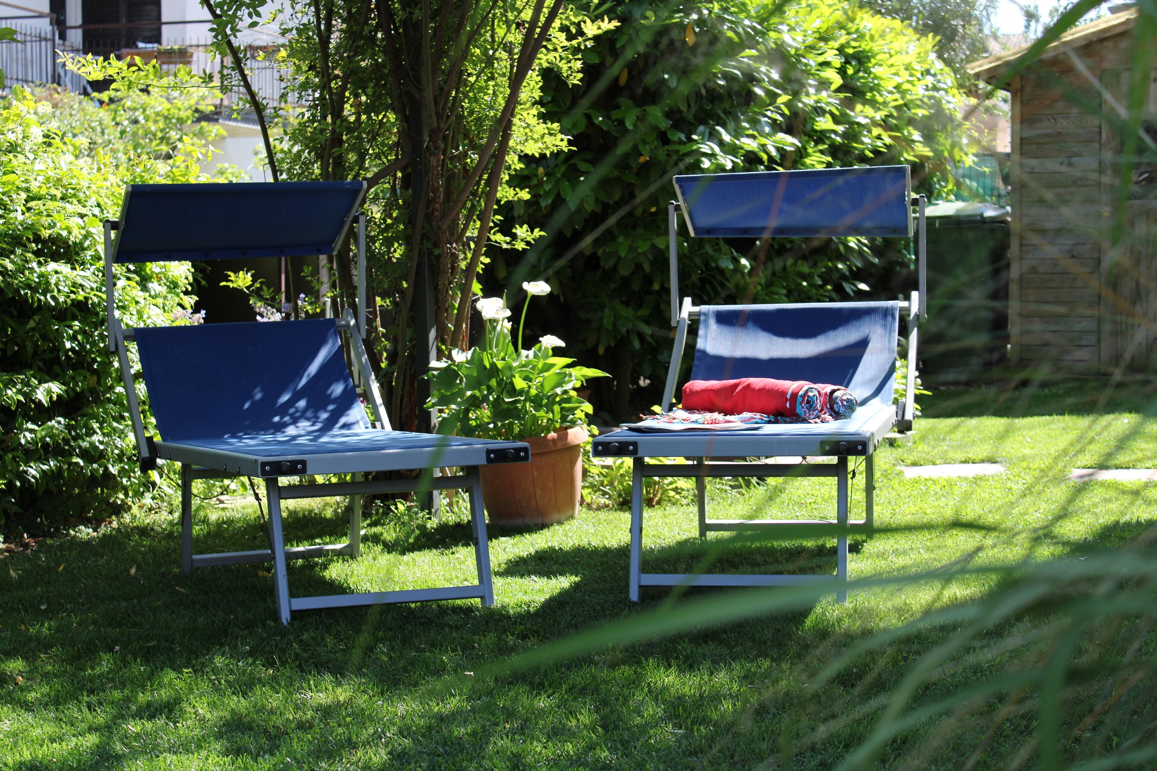 Due poltrone blu con parasole integrate in un'area giardino con prato e piante in vaso.