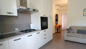 Moderni keittiö, jossa on valkoiset kaapit, liesi ja uuni. Keittiössä on myös ruokailutila, jossa on pöytä ja tuolit.