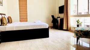 Habitación de hotel con cama, escritorio, silla, televisor y ventana con cortinas.