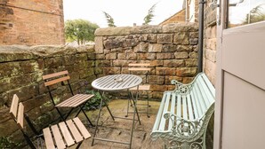 A patio area with a round table and two wooden chairs, a metal bench, and a stone wall. - Nine Ladies (Matlock)