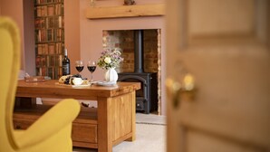 A wooden dining table with a bottle of wine, glasses, and a vase of flowers. A bookshelf and a fireplace are in the background. - Lime Kiln Farm, Malton, North York Moors (Malton)