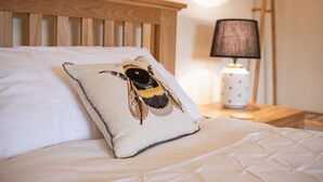 A bed with a pillow featuring a bee design, a wooden headboard, and a nightstand with a lamp. - Lime Kiln Farm, Malton, North York Moors (Malton)