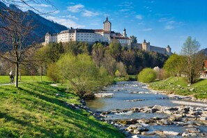 A castle on a hill overlooking a river with a cyclist on a path.