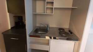 Una kitchenette pequeña y funcional con un fregadero, estufa y cajones para guardar cosas.