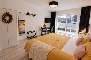 A bedroom with a bed, a desk, a chair, a TV, a window with curtains, and a wall-mounted sign.