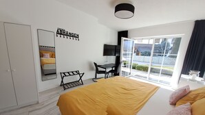 Un dormitorio con cama, armario, escritorio, silla y vistas al exterior.
