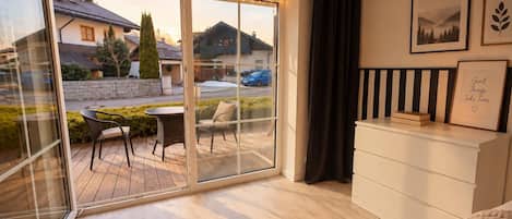 A modern bedroom with a sliding glass door leading to a balcony, a white dresser, and two framed pictures on the wall.