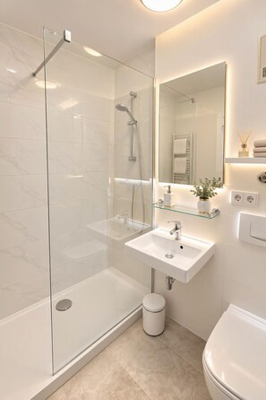 A modern bathroom with a glass-enclosed shower, a white sink, and a large mirror.
