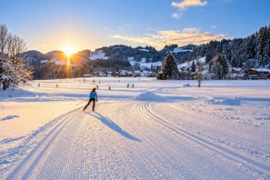 A cross-country skiing trail with a person skiing, surrounded by snow-covered trees and houses in the background. - Kampenwand Apartment (Aschau im Chiemgau)