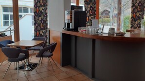 Un café moderno con un mostrador de madera, una máquina de café y una pizarra con la carta. Hay dos mesas con sillas.