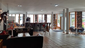 Un vestíbulo de hotel con mostrador de recepción, zona de estar y amplias ventanas.