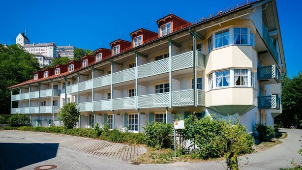 Un hotel de varios pisos con balcones, una habitación en esquina y un estacionamiento.