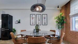 Un comedor con una mesa redonda, seis sillas, un refrigerador negro y una lámpara colgante.