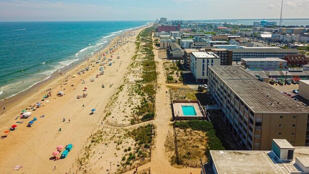 Ein Strand mit vielen Sonnenschirmen und Liegestühlen, einem Schwimmbad und einem Gebäude mit flachem Dach.