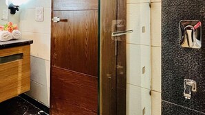 Un baño con puerta de madera, cabina de ducha de vidrio, pared de azulejos y un perchero con toallas.
