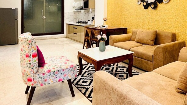 Una sala moderna con un sofá, un sillón floral, una mesa de centro y un comedor con mesa y sillas.