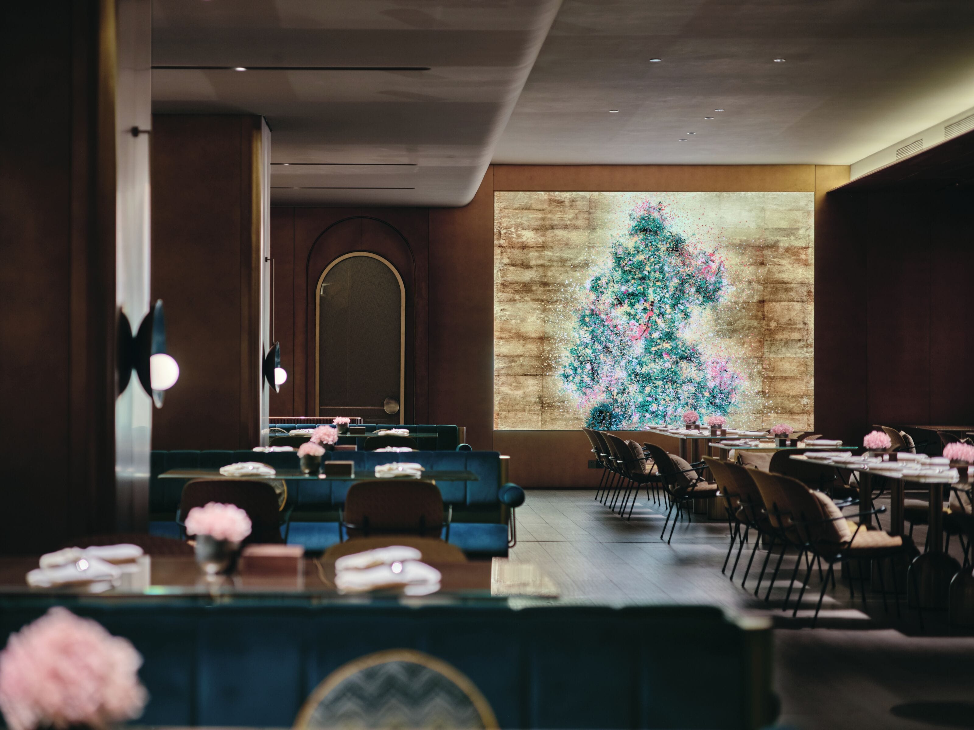 Een restaurant met een lange toonbank, meerdere tafels en stoelen. Een groot projectiescherm toont een bloemmotief op de muur.