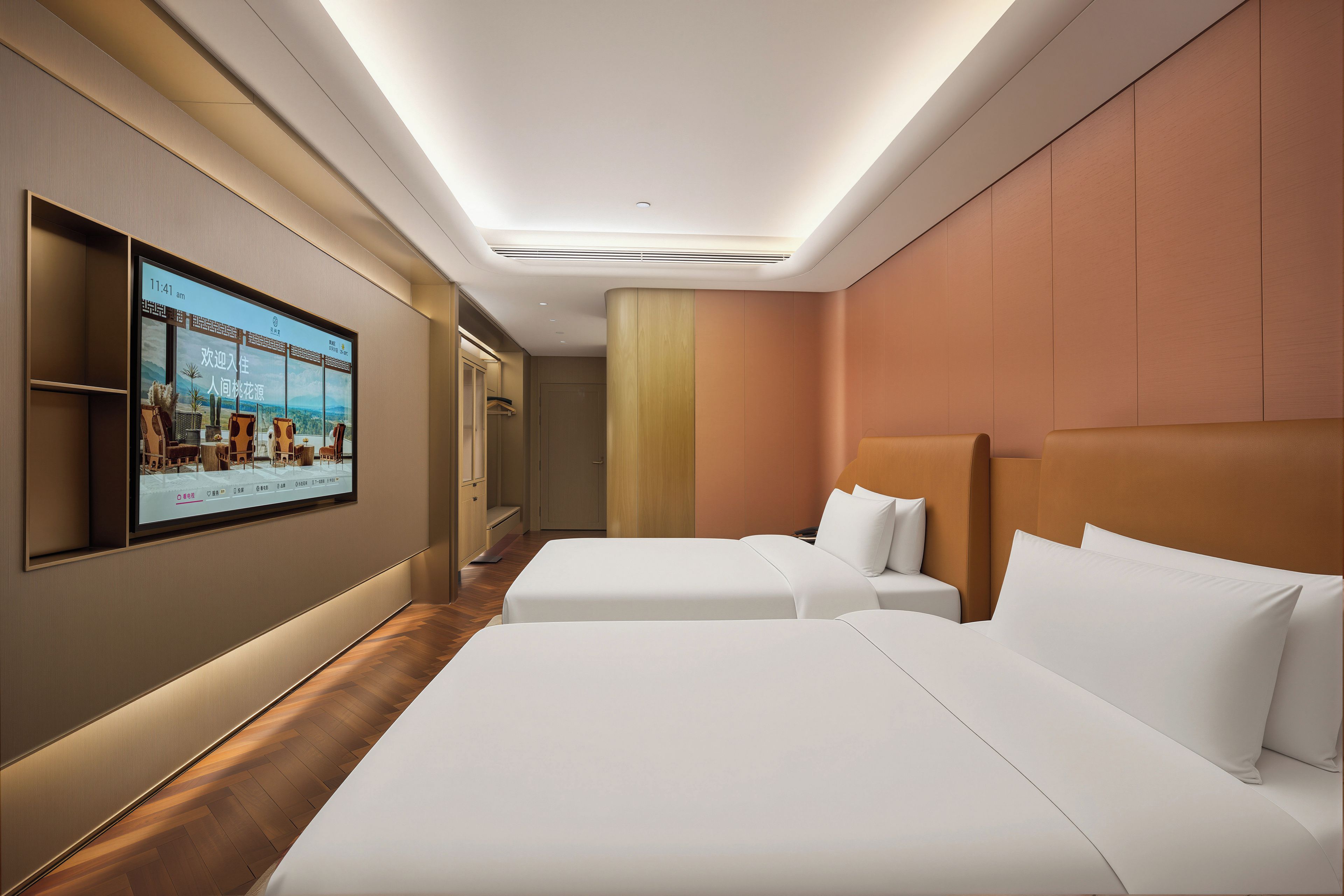 Ein Hotelzimmer mit zwei Betten, einem an der Wand befestigten Fernseher und Holzboden.