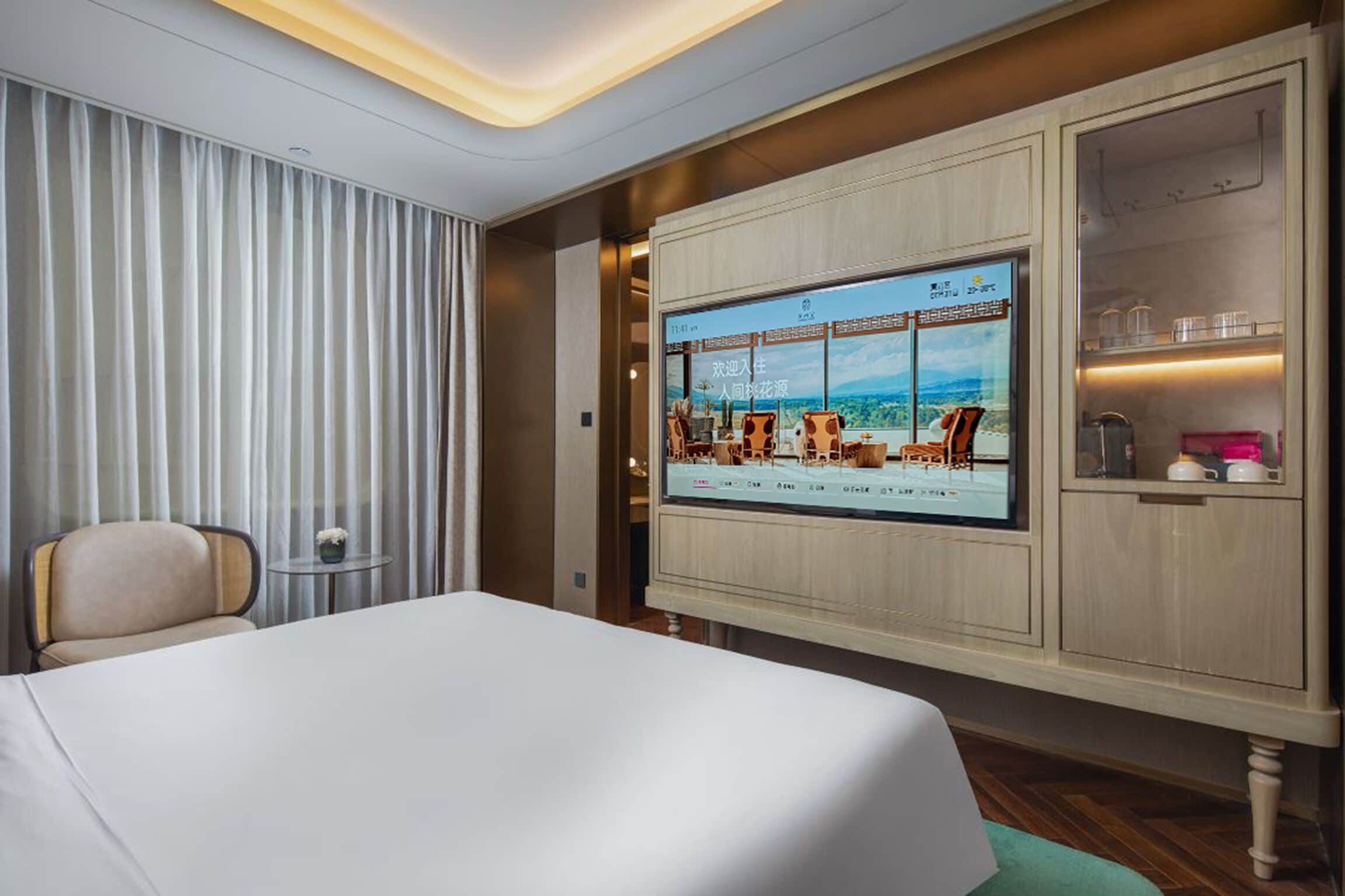A hotel room with a bed, a television mounted on the wall, a chair, and a small table.