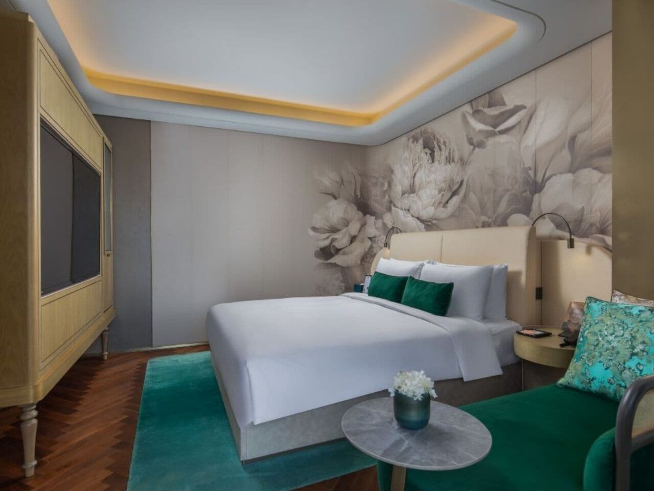 A hotel room with a bed, a green sofa, a small round table, and a wall with a floral mural.