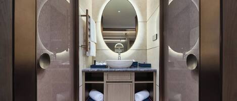 A modern bathroom with a central sink, a large mirror, and two towel racks.