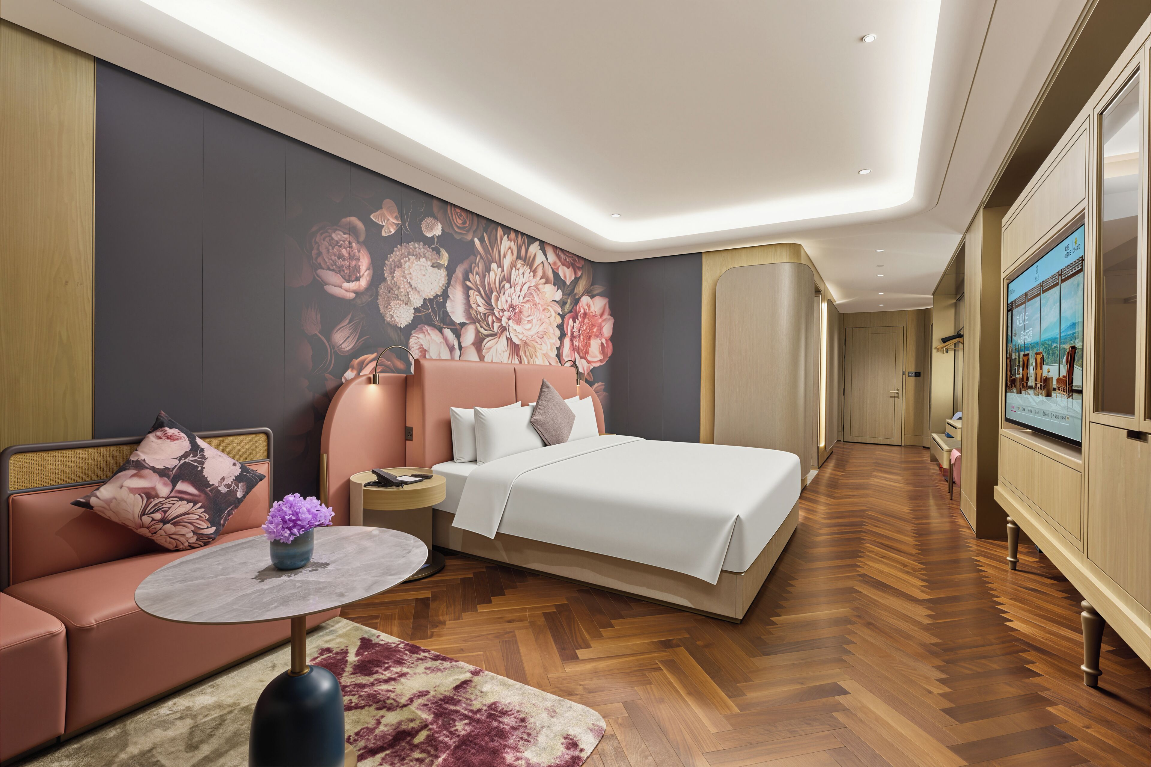 A modern hotel room with a large bed, a sofa, a small table with a vase, and a television on the wall.