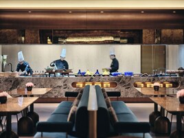 Un ristorante moderno con un bancone in marmo, cuochi con cappello e una fila di tavoli con sedie.