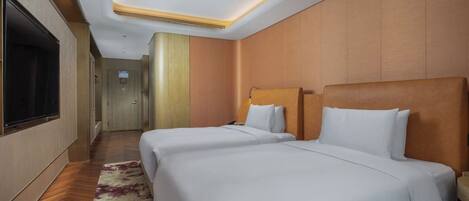 A hotel room with two beds, a TV, and a hallway leading to other rooms.