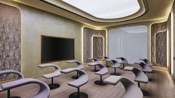 A modern room with curved seating, a large flat-screen TV, and a large window.