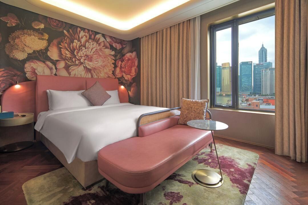 Una habitación de hotel moderna con una cama grande, vistas a la ciudad y un mural floral en la pared.