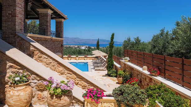 A pool area with a view of the sea, surrounded by potted plants and a wooden fence.