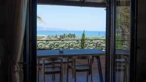 A balcony with a table and chairs, overlooking a coastal landscape with trees and the sea.