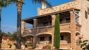 A stone building with a balcony, a palm tree, and potted plants.