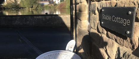 Un muro de piedra con un letrero que dice "Stable Cottage" y una mesa metálica blanca junto a una silla metálica.