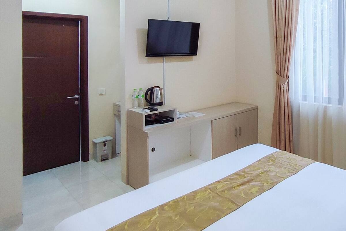 Habitación de hotel con cama, televisor en la pared, escritorio con cafetera y ventana con cortinas.