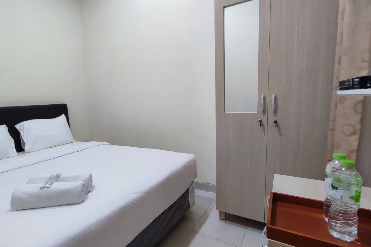 Habitación de hotel con cama, armario y una mesita con una botella de agua.