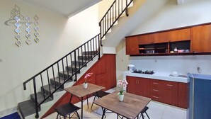 A kitchen with wooden cabinets, a stove, and a dining area with two tables and chairs. - Atmosfer Guest House Sentul by Ruang Nyaman (Sentul City)