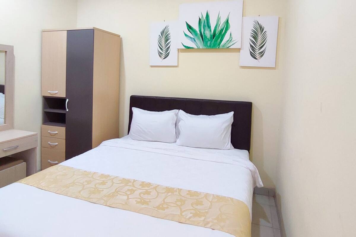 Habitación de hotel con cama, armario, escritorio y espejo. Tres obras de arte en la pared representan hojas.