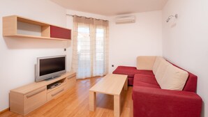 Una sala de estar moderna con televisor de pantalla plana, muebles de madera, un sofá rojo y una ventana con cortinas.