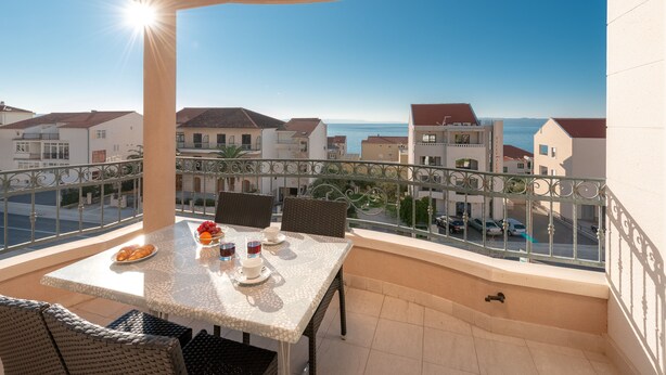 Un balcón con una mesa lista para dos personas, con vistas a la costa, edificios y el mar.