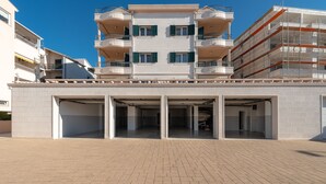 Un edificio de varios pisos con una entrada central, balcones y un estacionamiento.