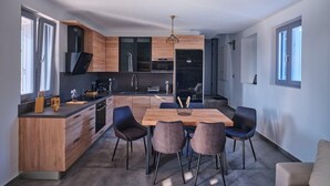 A modern kitchen with a central island, dark cabinetry, and a dining area with four chairs. - OLEA VILLA (NAOUSA)