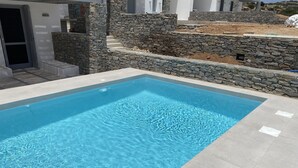 A rectangular swimming pool with clear blue water, surrounded by stone walls and a tiled deck. - OLEA VILLA (NAOUSA)